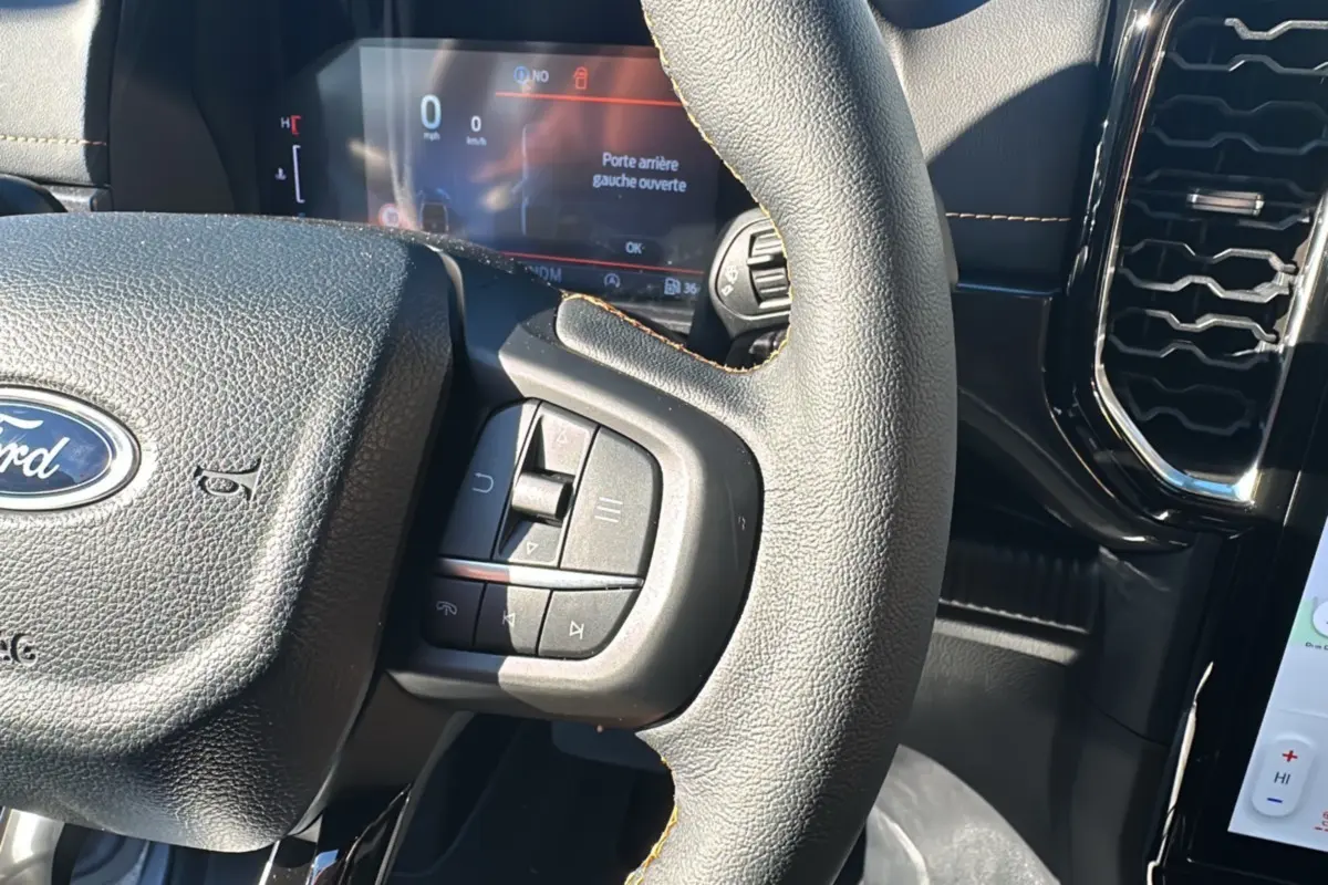 Vue rapprochée du volant cuir multifonctions noir du Ford Ranger Wildtrak 2026 avec tableau de bord digital allumé.