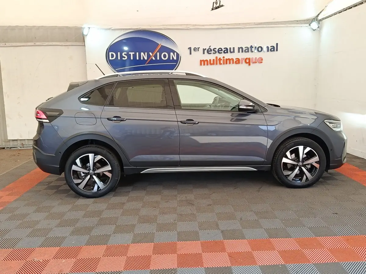Vue de profil côté droit d'un Volkswagen Taigo gris foncé 2023 avec jantes alliage et barres de toit chromées.