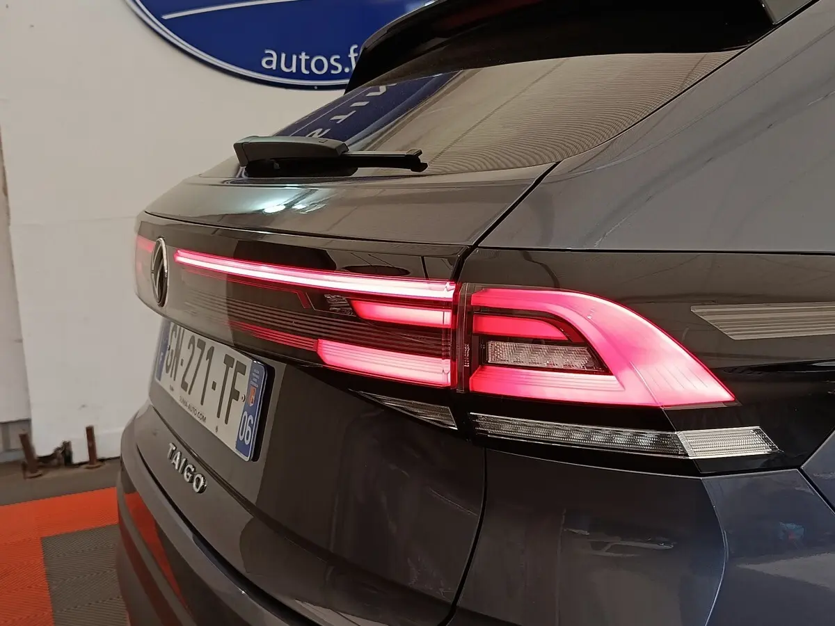 Vue arrière droite du Volkswagen Taigo gris foncé 2023 avec feux arrière LED allumés et logo visible.