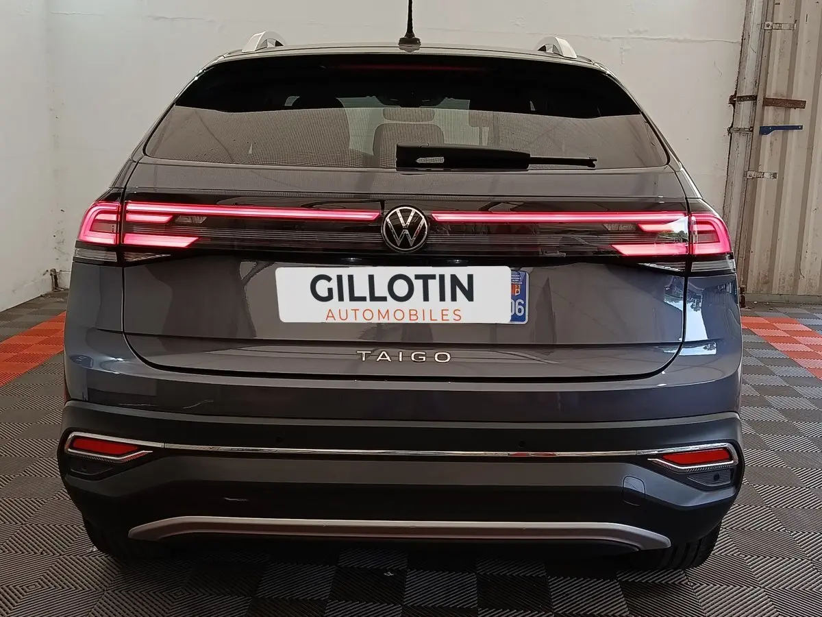 Vue arrière d’un Volkswagen Taigo gris foncé 2023 avec feux arrière LED allumés dans un garage.