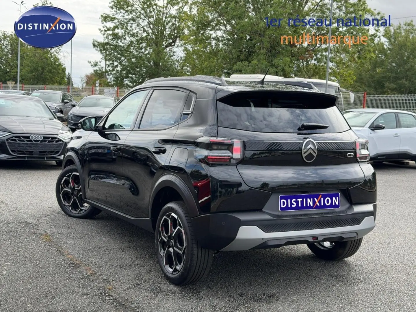 Vue 3/4 arrière d'une Citroën C3 noire 2025 avec jantes noires et détails rouges, stationnée en extérieur sur parking.