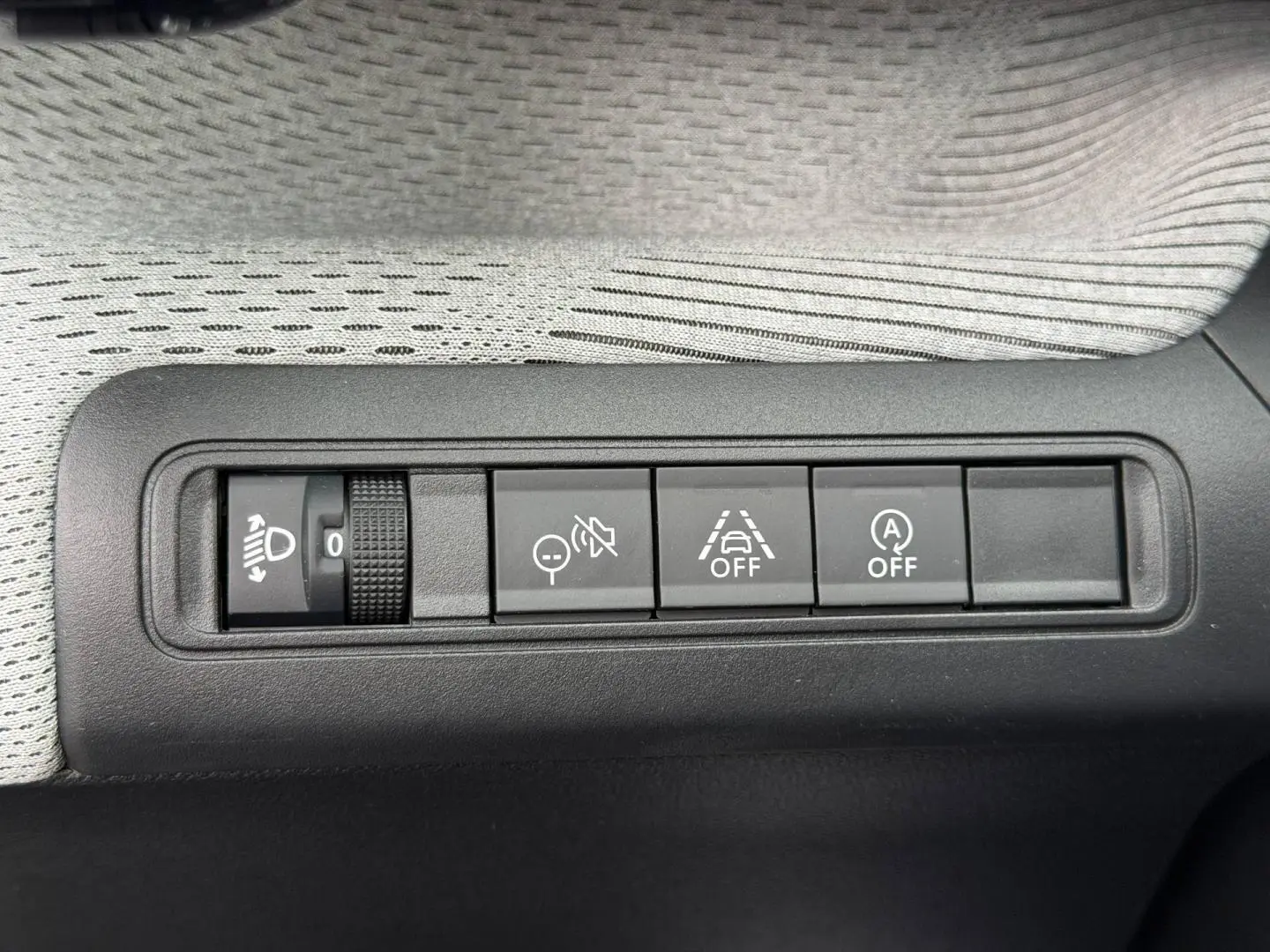 Gros plan sur les commandes de réglage des phares et d'assistance à la conduite dans une Citroën C3 noire, version 2025.
