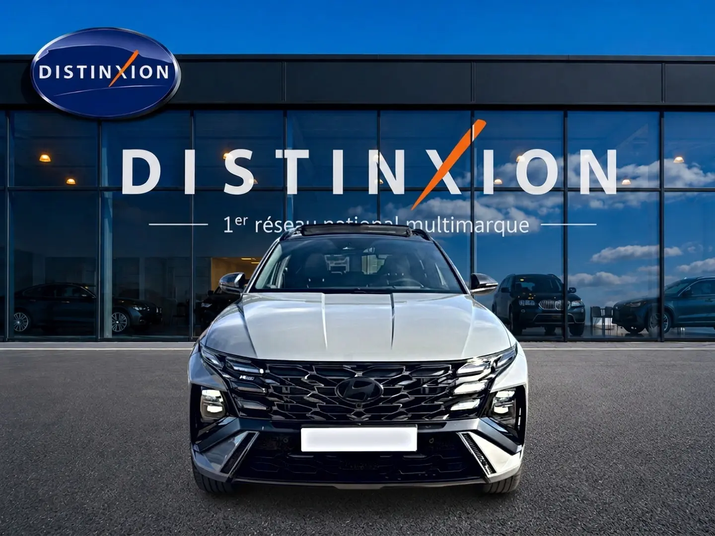 Vue avant du Hyundai Tucson gris shadow avec calandre noire et phares LED, devant une vitrine Distinxion.