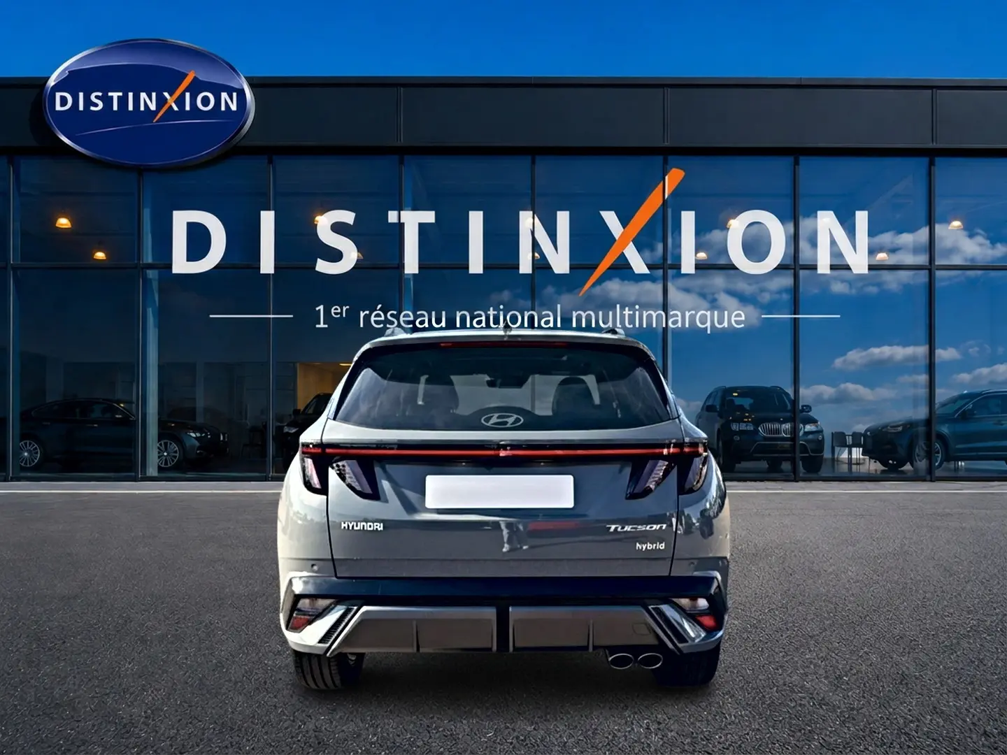 Vue arrière du Hyundai Tucson gris shadow hybride, avec feux LED et double sortie d'échappement visible devant une vitrine Distinxion.