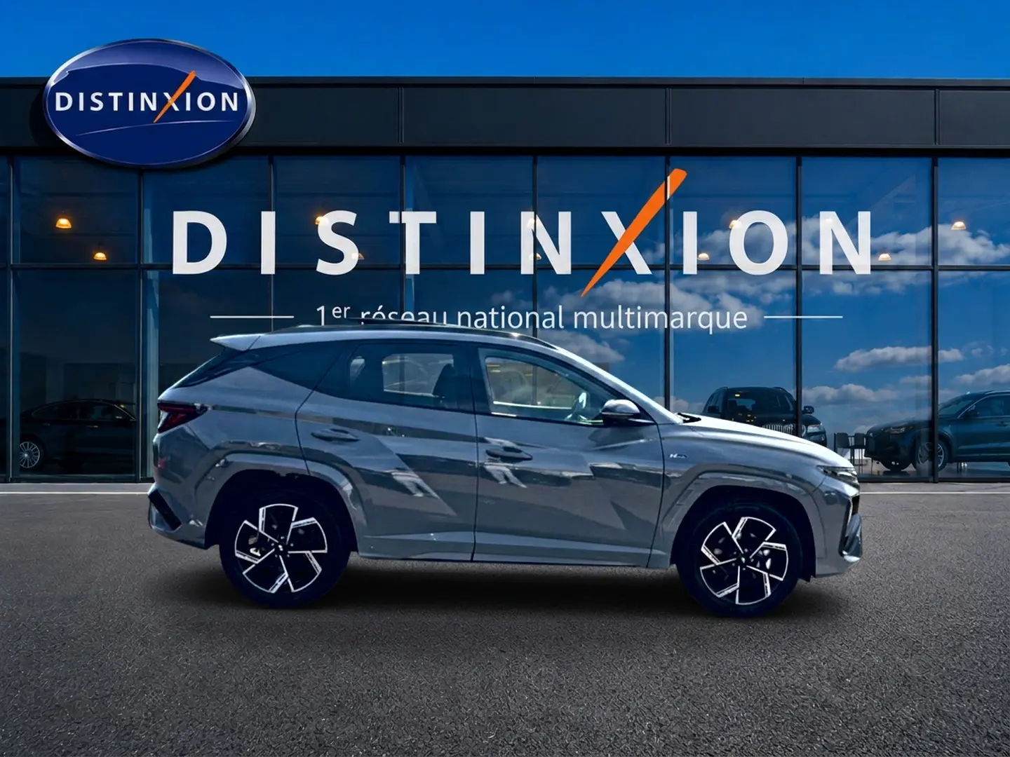 Hyundai Tucson 2026 gris shadow en profil droit devant une vitrine avec logo Distinxion.