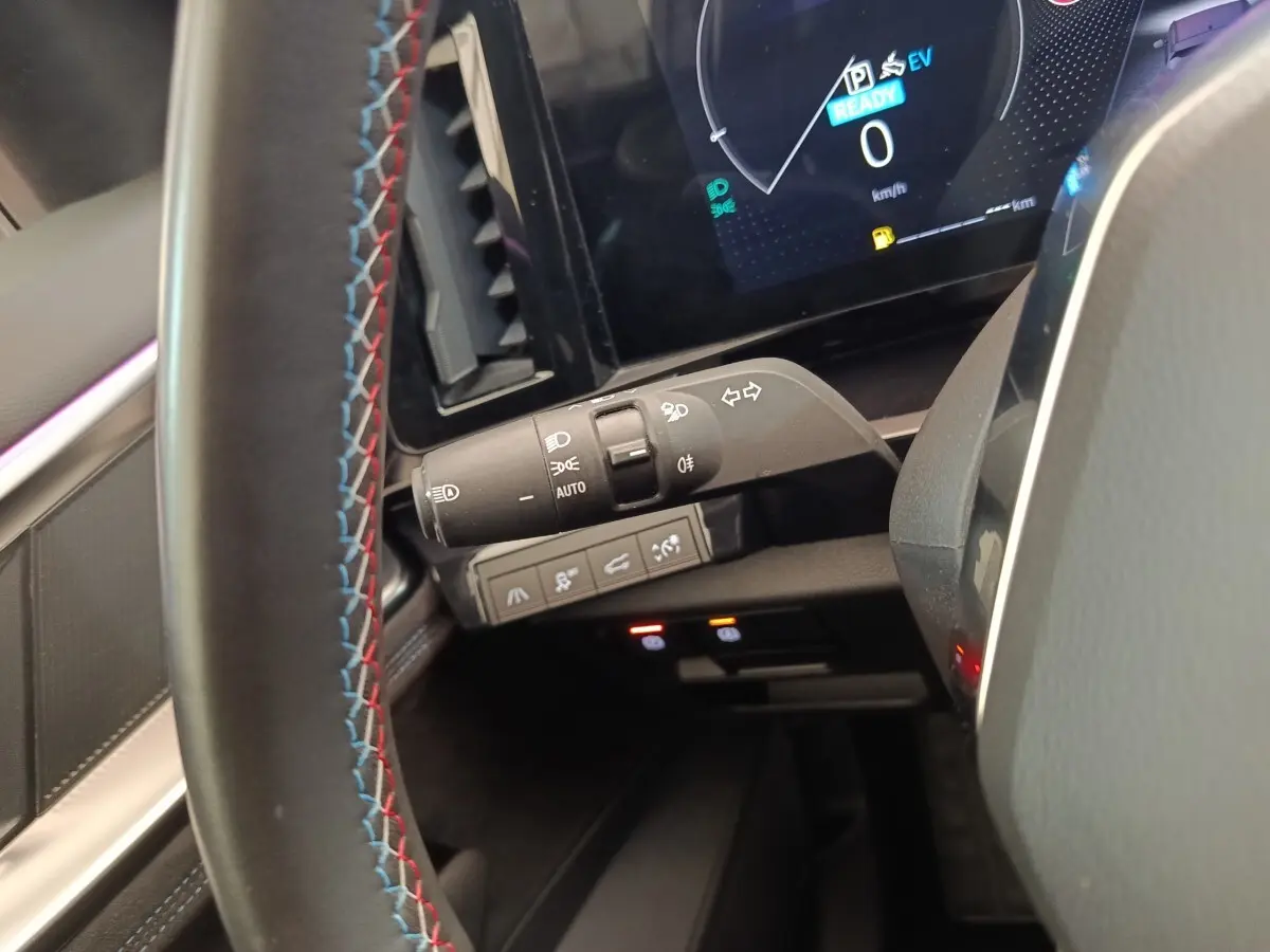 Gros plan intérieur sur la manette de feux et le volant suédé tricolore du Renault Austral gris clair 2024.