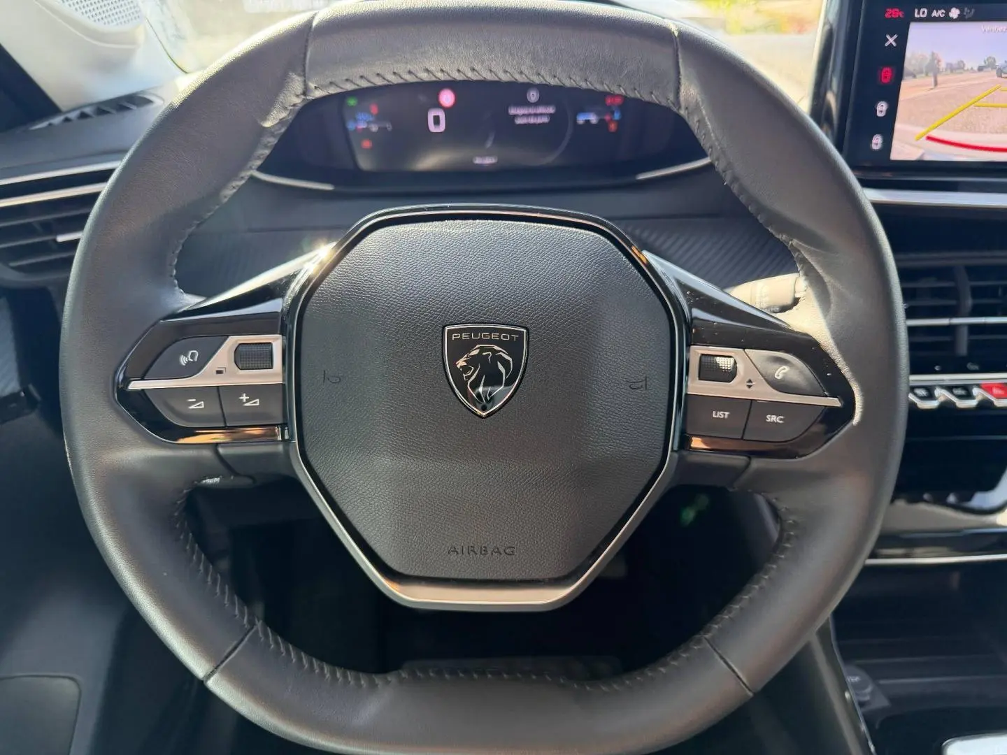 Vue rapprochée du volant cuir noir de la Peugeot 208 2025 avec commandes intégrées et logo lion central.