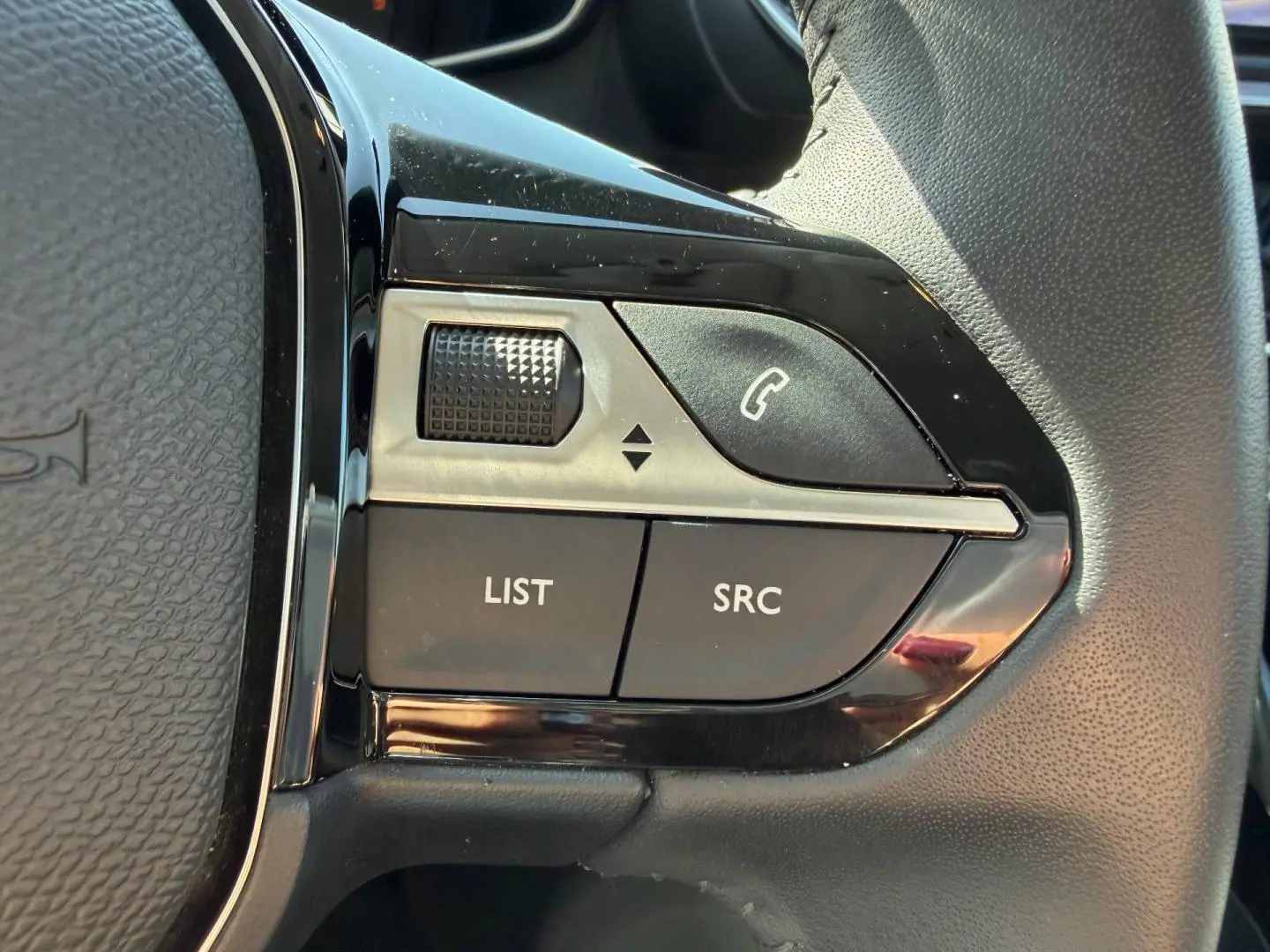 Gros plan sur les commandes audio au volant noir brillant de la Peugeot 208 gris Artense, version 2025.