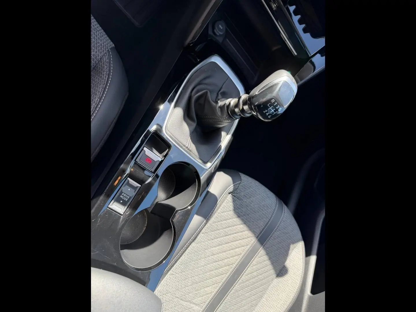 Gros plan sur la console centrale intérieure de la Peugeot 208 2025, avec levier de vitesse manuel et siège tissu gris clair.