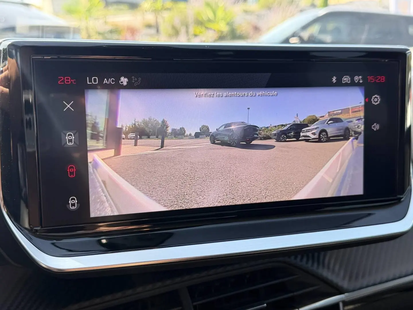 Écran tactile intérieur montrant la caméra de recul avec vue arrière sur un parking ensoleillé.