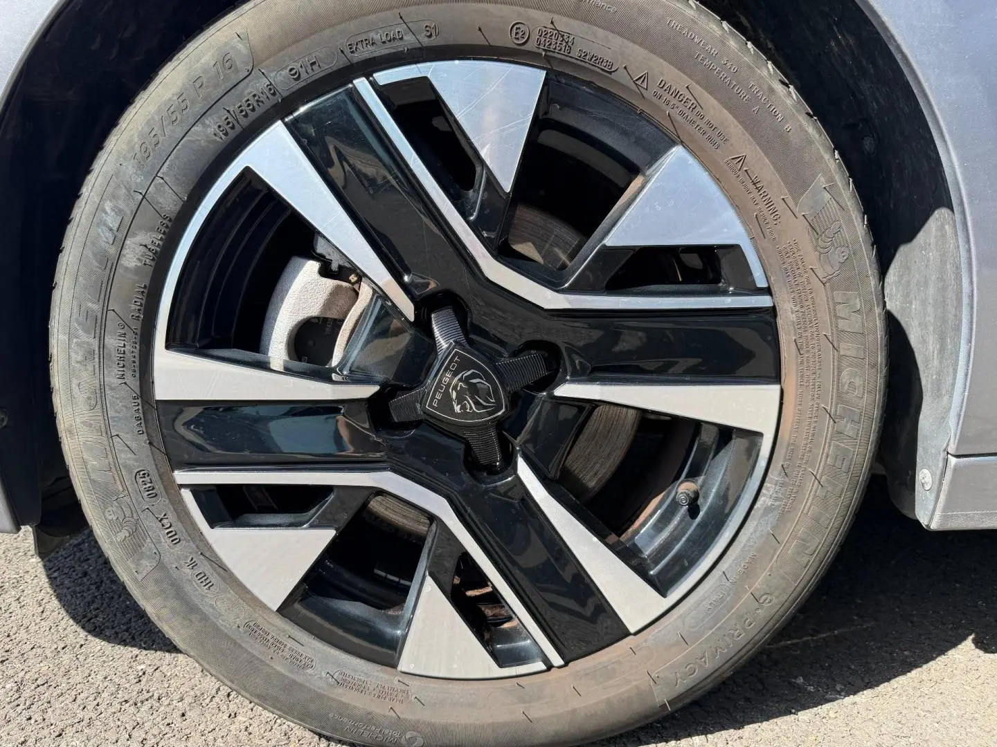 Gros plan sur la jante alu bicolore noire et argentée d'une Peugeot 208 Gris Artense, roue avant droite visible.