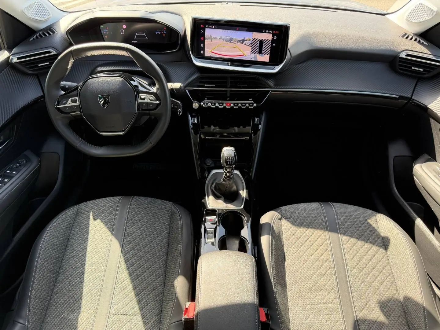 Vue intérieure de face du poste de conduite de la Peugeot 208 gris Artense, volant compact et écran tactile avec caméra de recul.