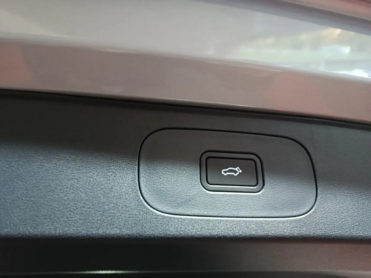 Gros plan sur le bouton d'ouverture électrique du coffre, entouré de plastique noir, sur un véhicule gris clair Geely STARRAY.