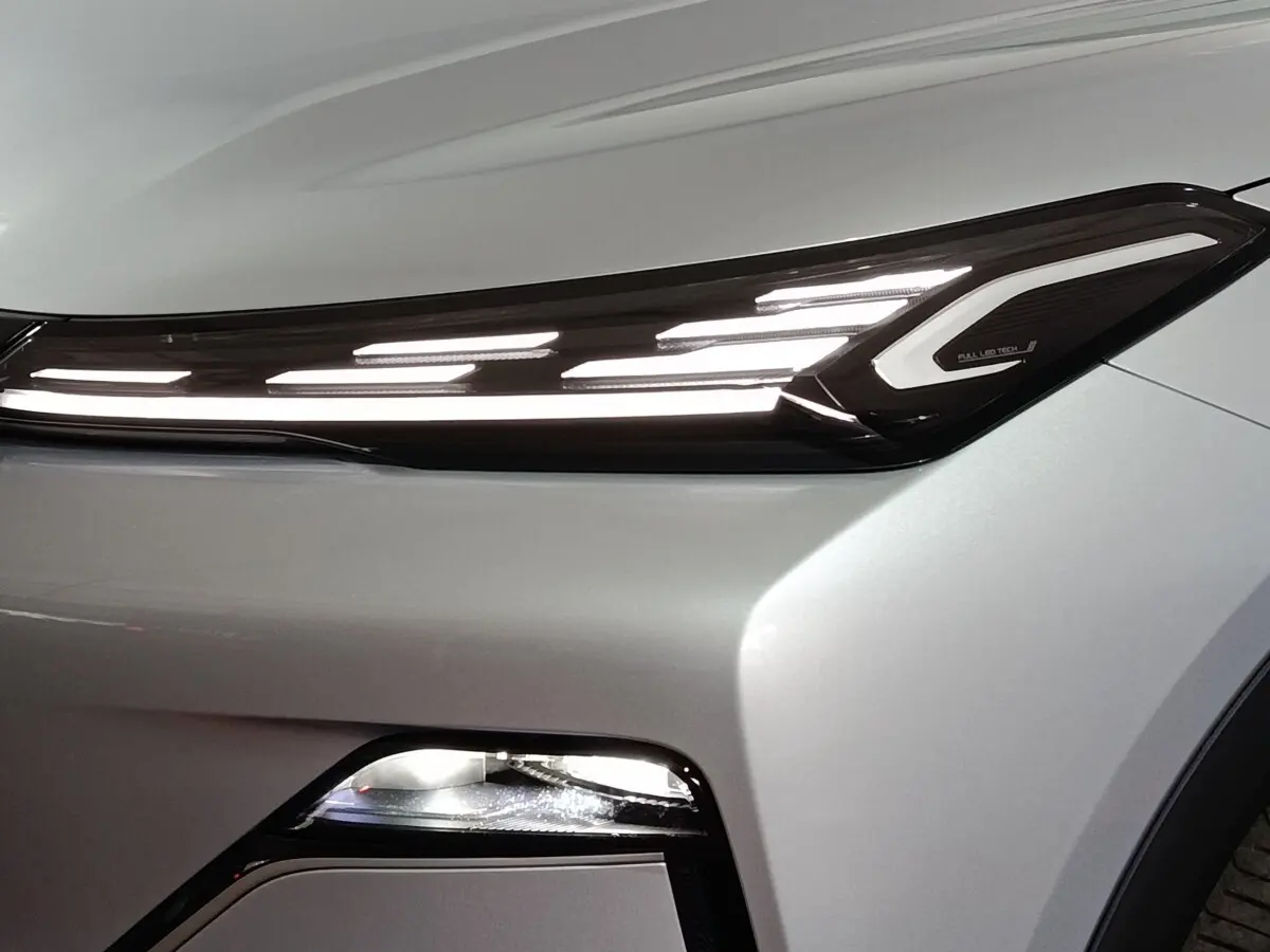 Gros plan sur le phare avant droit allumé d’un Geely STARRAY gris clair avec éclairage LED distinctif en bandeau.