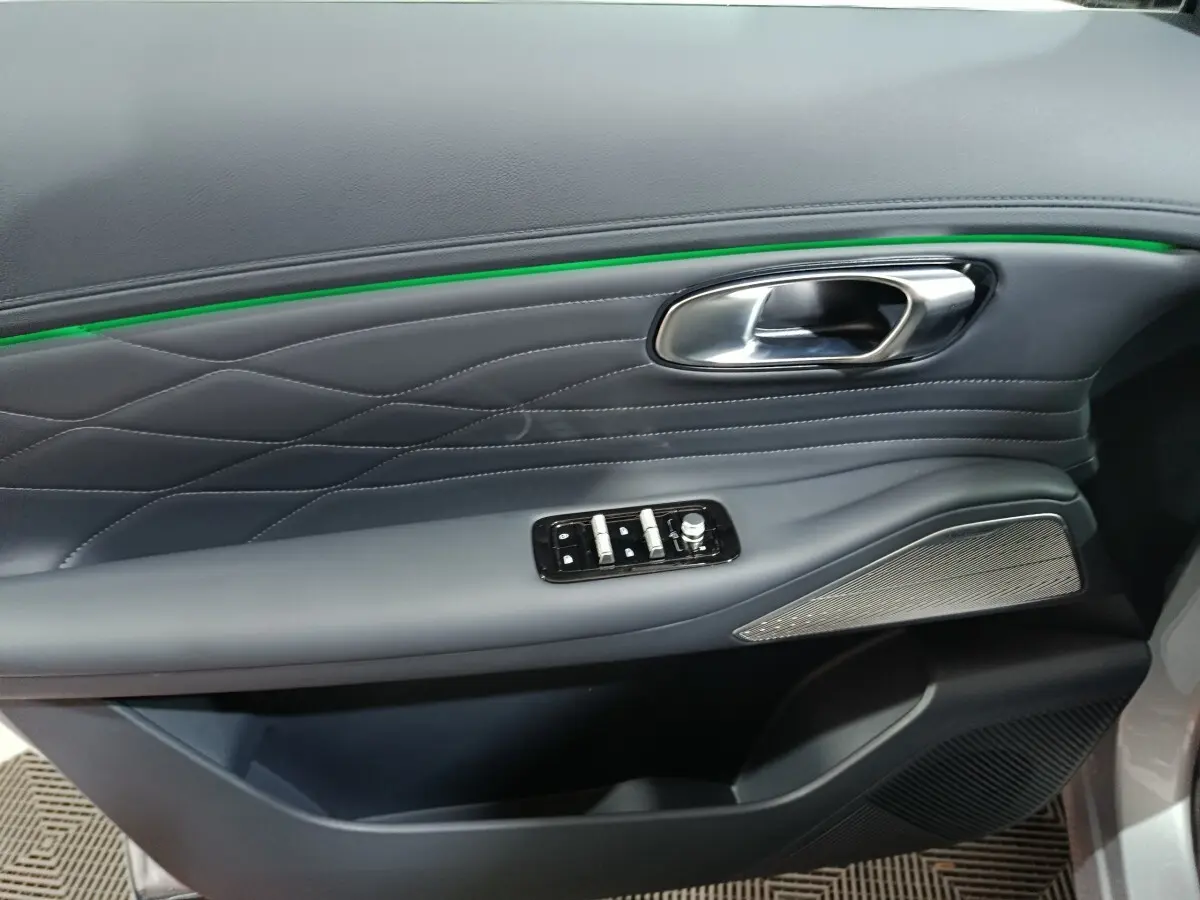 Gros plan sur la porte côté gauche gris clair du Geely STARRAY 2026, avec surpiqûres, bande lumineuse verte et commandes électriques.