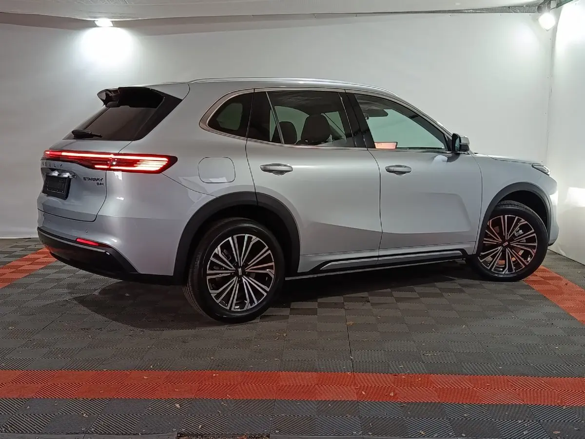Vue de profil côté droit du SUV GEELY STARRAY gris clair avec feux arrière allumés dans un studio lumineux.