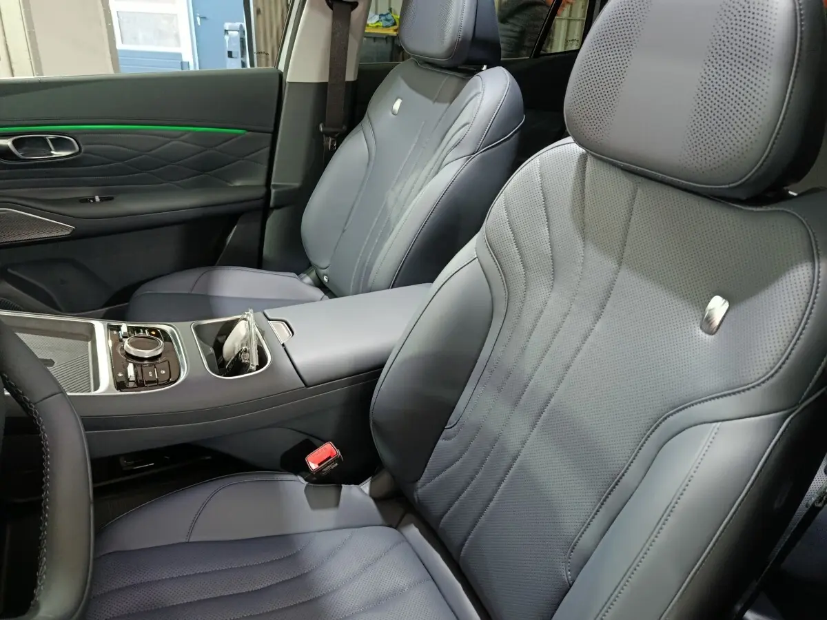 Vue intérieure rapprochée des sièges avant gris foncé en cuir perforé du GEELY STARRAY 1.5 EM-I PHEV Max+ avec accoudoir central.