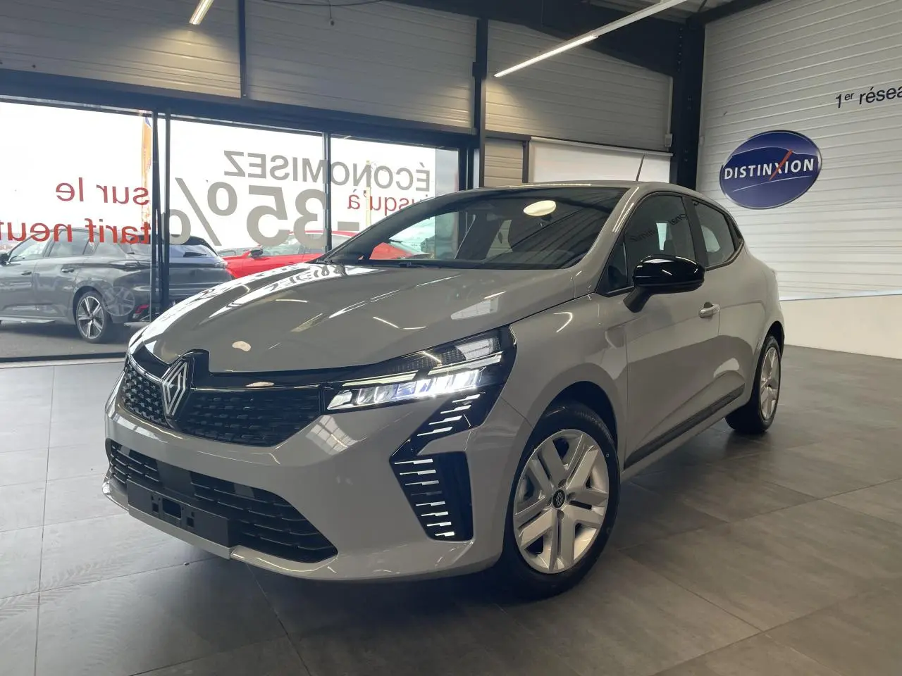 Renault Clio 1.5 Blue dCi 2025 gris Rafale vue 3/4 avant en intérieur avec phares LED allumés et jantes argentées.