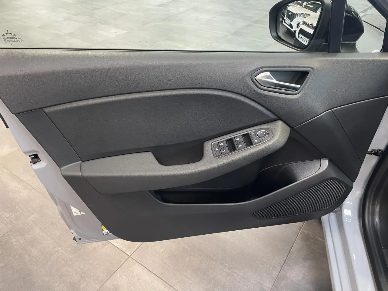 Vue intérieure côté gauche de la porte avant gris rafale de la Renault Clio 2025 avec commandes de vitres et rétroviseur.