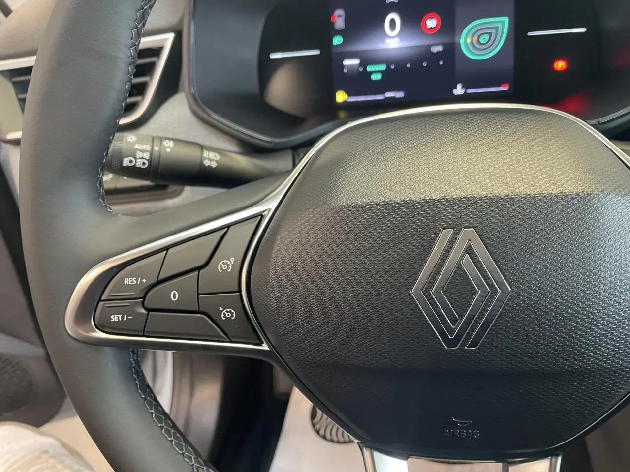 Gros plan sur le volant noir texturé avec logo Renault chromé et commandes de régulateur de vitesse sur la gauche.