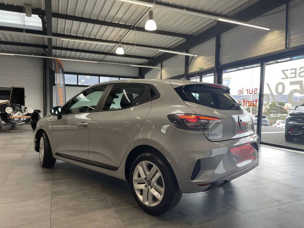 Vue 3/4 arrière droite d'une Renault Clio 1.5 Blue dCi 2025 gris Rafale avec feux LED et jantes alliage en showroom.