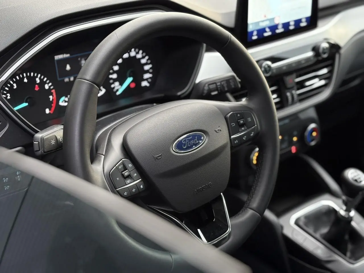 Vue intérieure rapprochée du volant en cuir multifonctions du Ford Kuga 2024 avec tableau de bord et console centrale visibles.