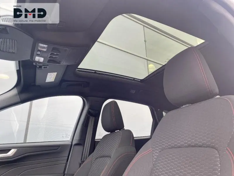 Intérieur du Ford Kuga blanc Glacier, vue avant des sièges ST-Line avec toit ouvrant panoramique et surpiqûres rouges.