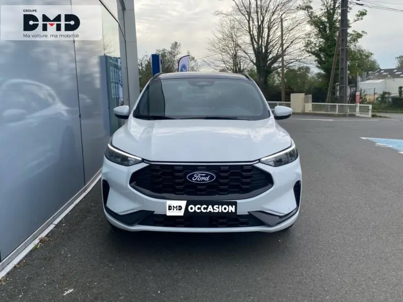 Vue avant d'un Ford Kuga blanc Glacier avec calandre noire hexagonale et phares LED fins, stationné devant un bâtiment.