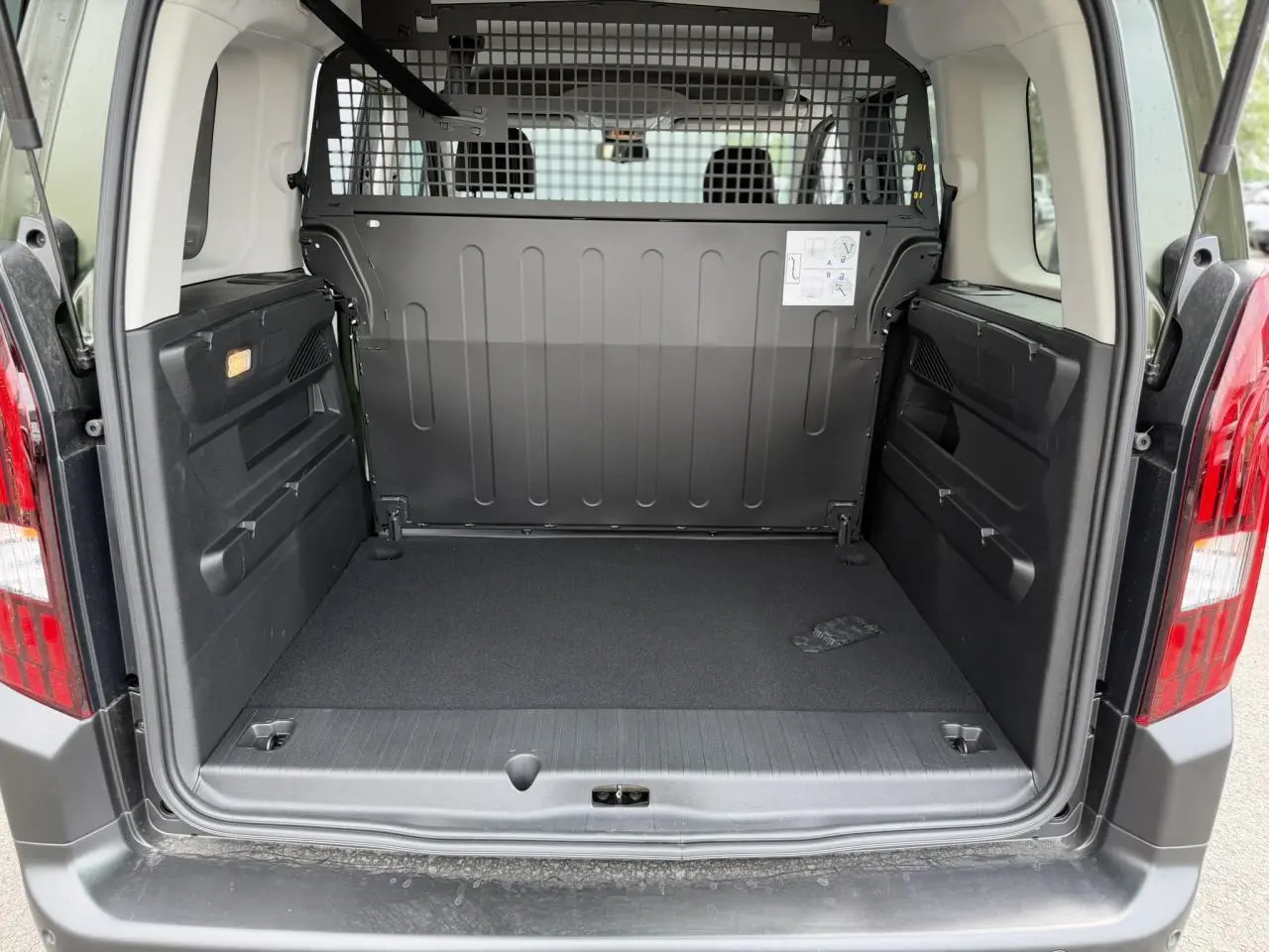 Coffre ouvert vu de l'arrière du Peugeot Rifter vert Sirkka, montrant l'espace de chargement et la grille de séparation.