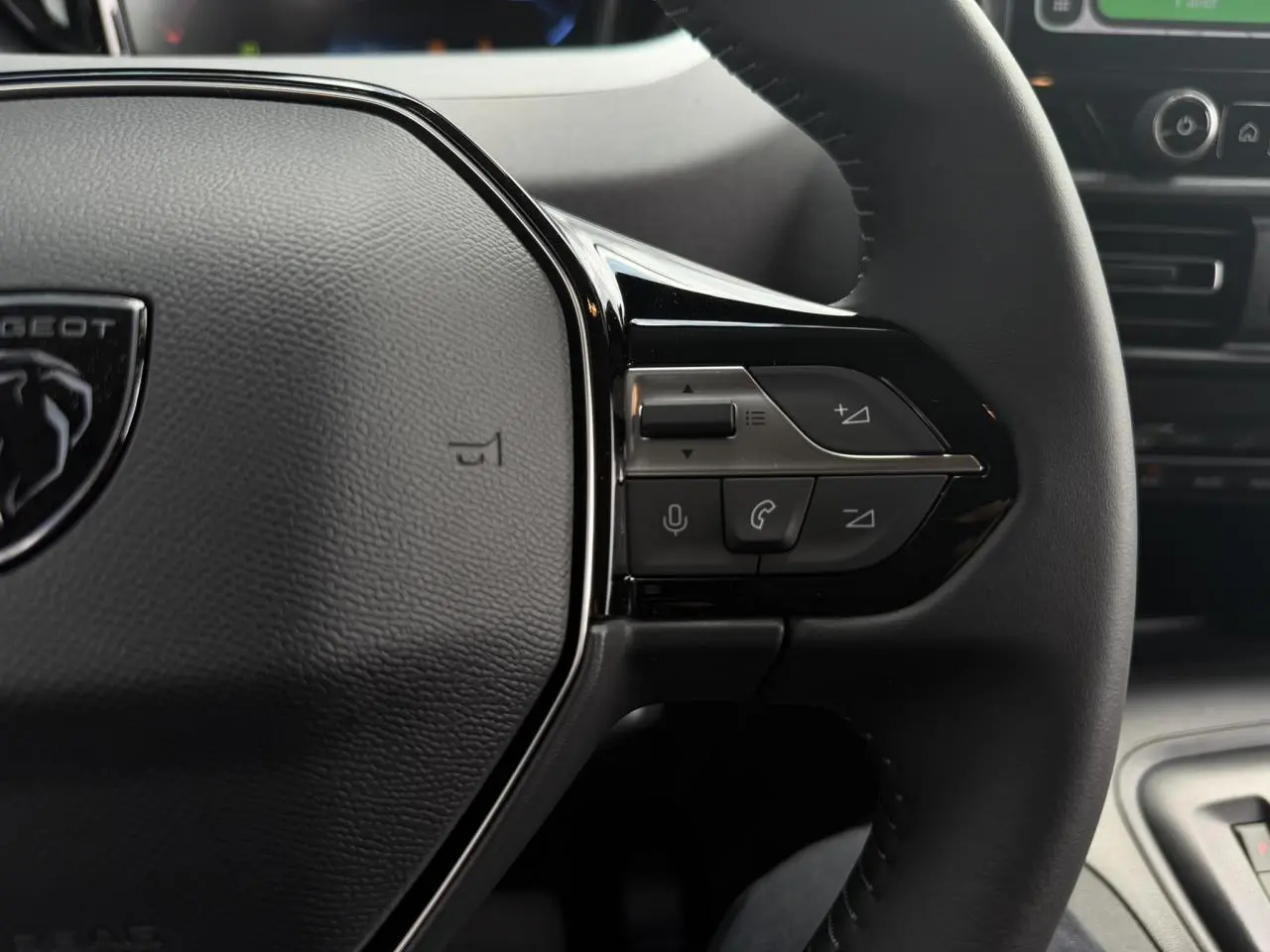 Gros plan sur le volant cuir multifonction du Peugeot Rifter 2026, boutons de commande audio et téléphone visibles.