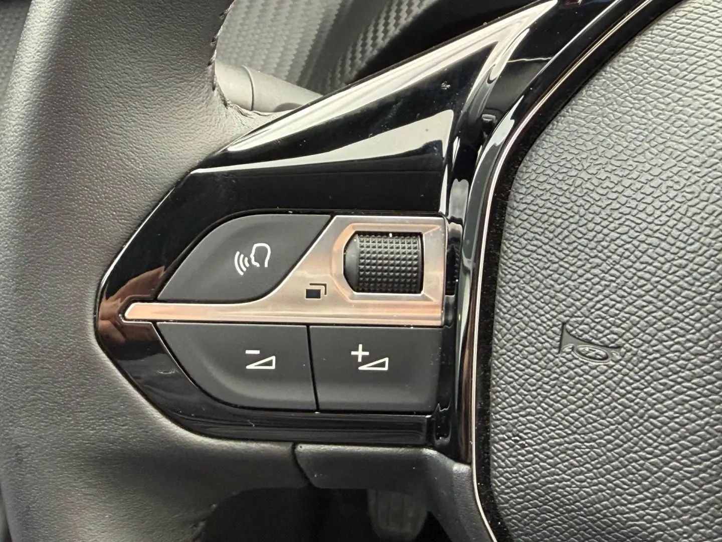 Gros plan sur les commandes audio au volant noir brillant de la Peugeot 208 1.2 100ch Allure 2025.