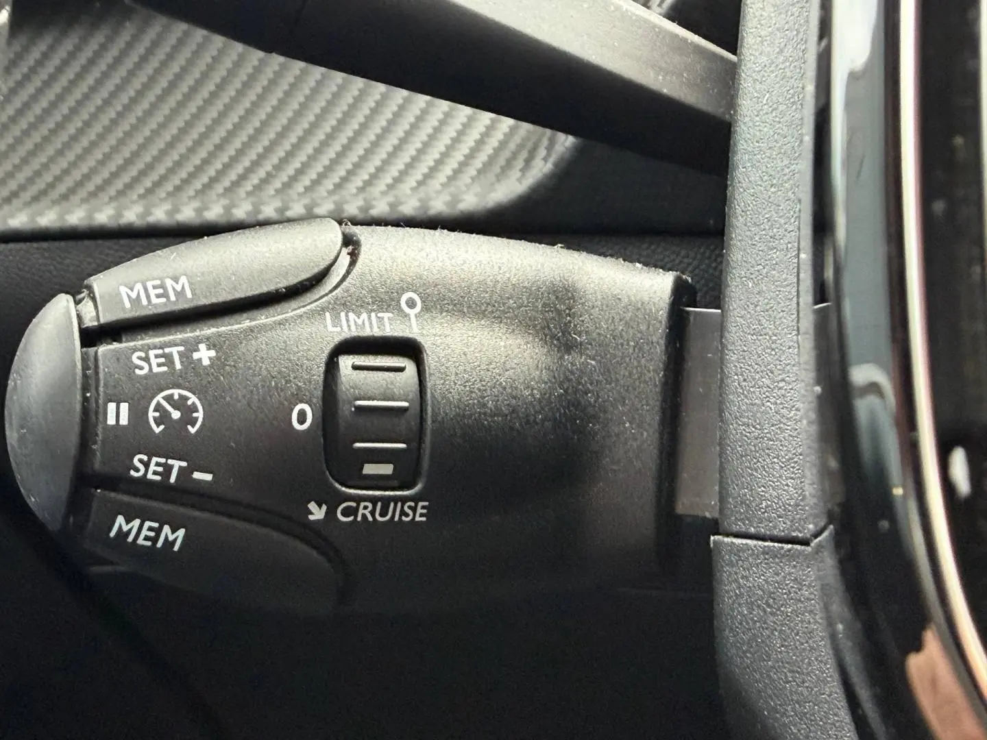 Gros plan sur la commande de régulateur de vitesse noire à gauche du volant dans une Peugeot 208 noire Perla Nera 2025.