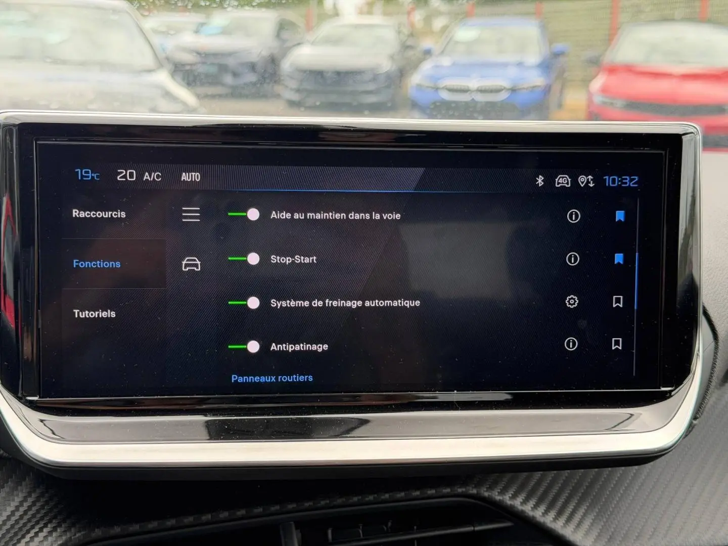 Écran tactile intérieur de la Peugeot 208 2025 affichant les aides à la conduite, avec reflet de voitures en arrière-plan.