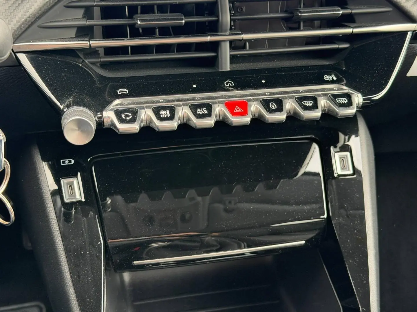 Vue rapprochée de la console centrale noire brillante du Peugeot 208 1.2 100ch Allure avec boutons chromés et touches fonctionnelles.