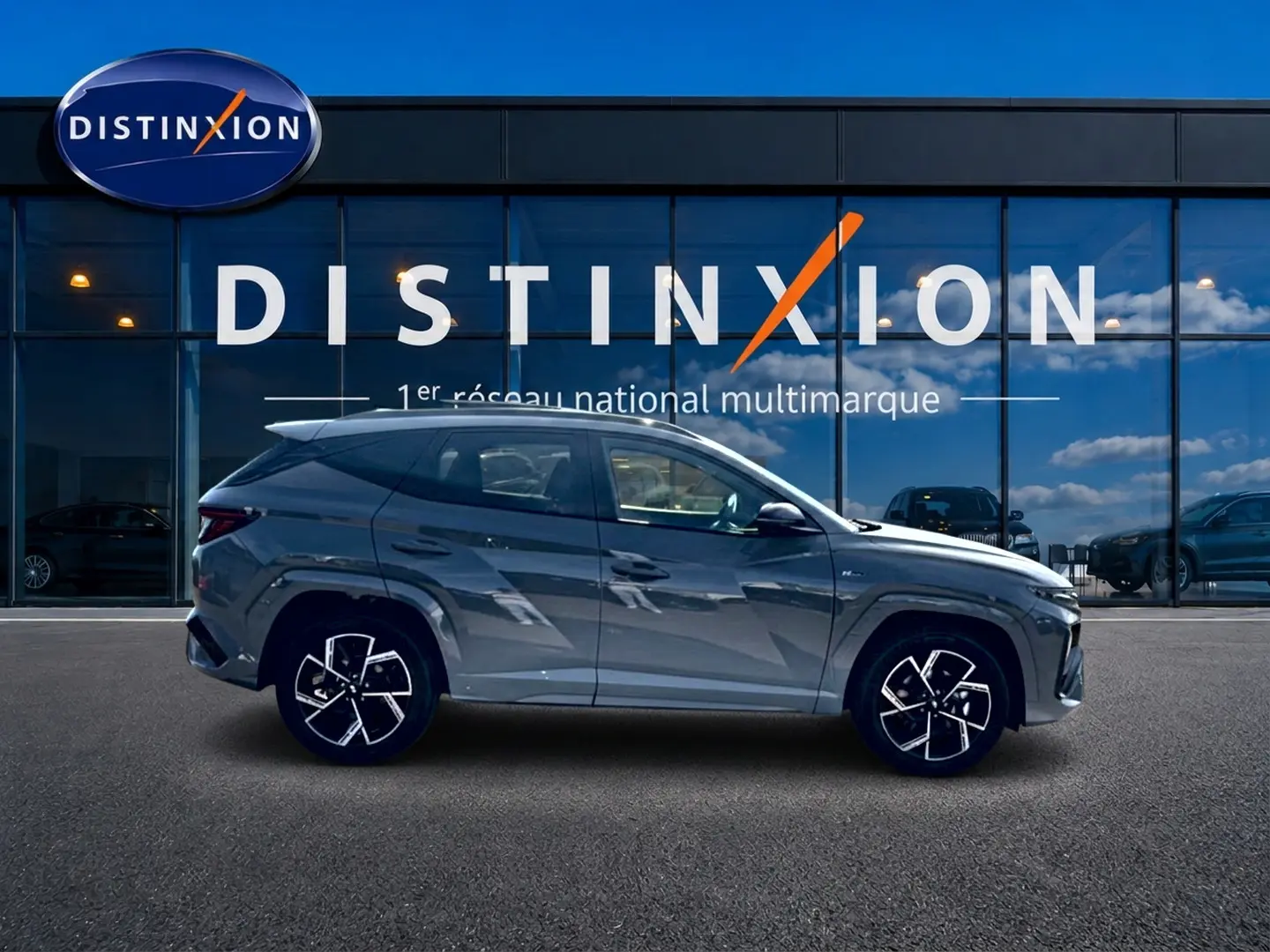 Vue de profil côté gauche du Hyundai Tucson 2026 gris shadow avec jantes alliage distinctives devant un showroom Distinxion.