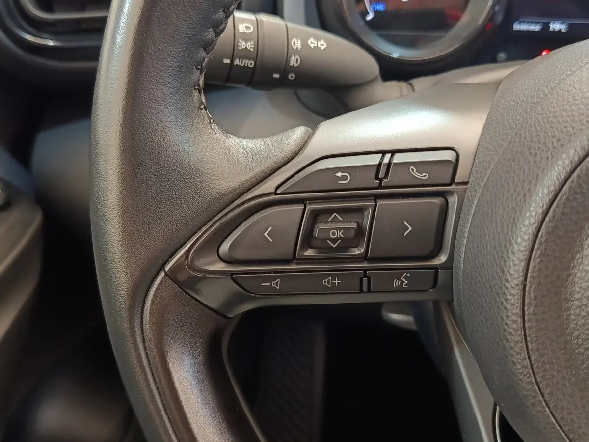 Gros plan sur les commandes multifonctions du volant cuir noir de la Toyota Yaris Hybride 116h Collection 2022.