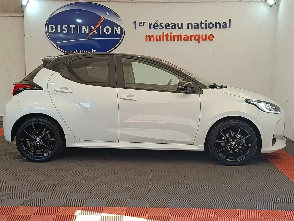 Profil droit d'une Toyota Yaris hybride blanche 2022 avec jantes noires et toit noir, en intérieur showroom.
