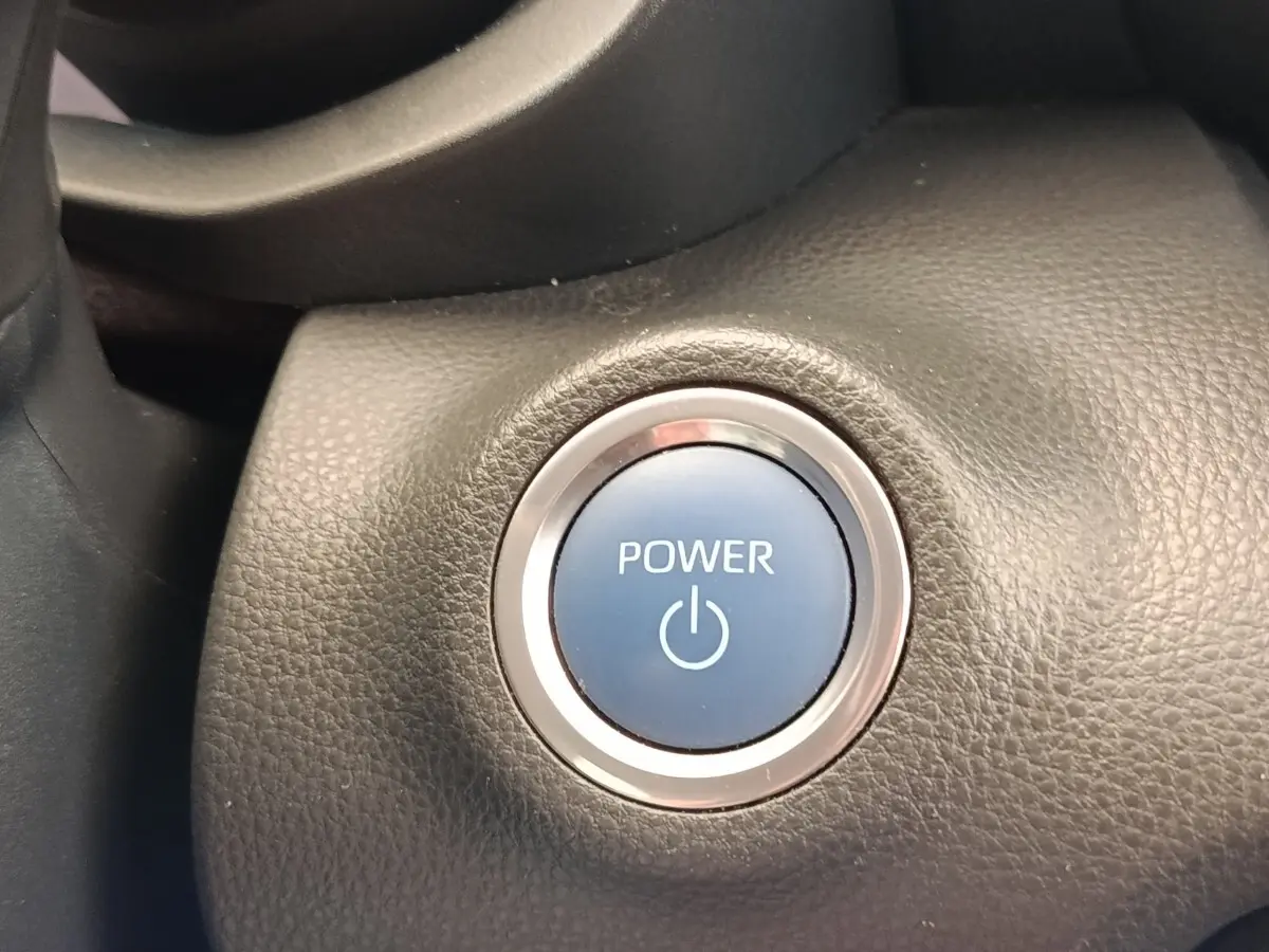 Gros plan sur le bouton démarrage Power bleu entouré de chrome dans l’habitacle noir d’une Toyota Yaris hybride 2022.