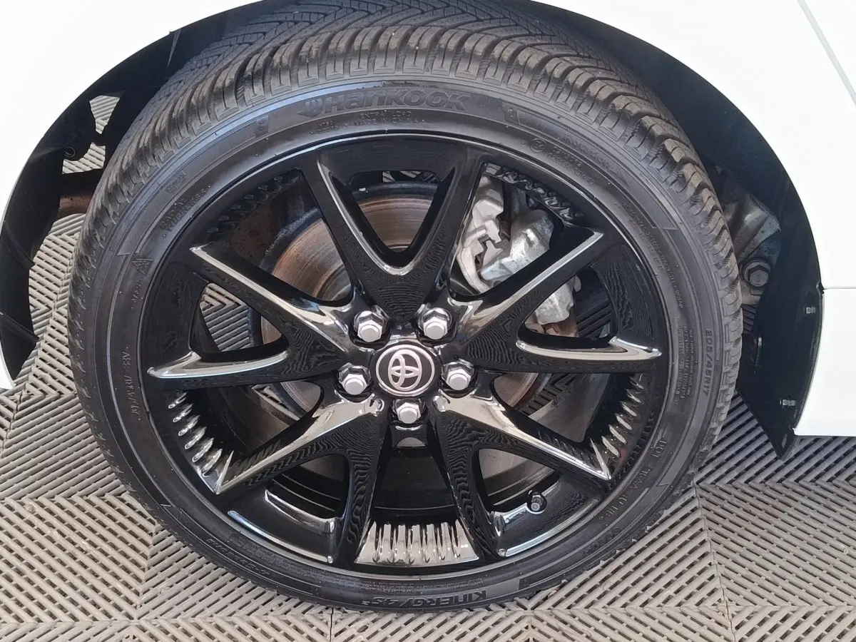 Gros plan sur la roue avant droite noire brillante d'une Toyota Yaris hybride blanche, avec logo Toyota au centre.