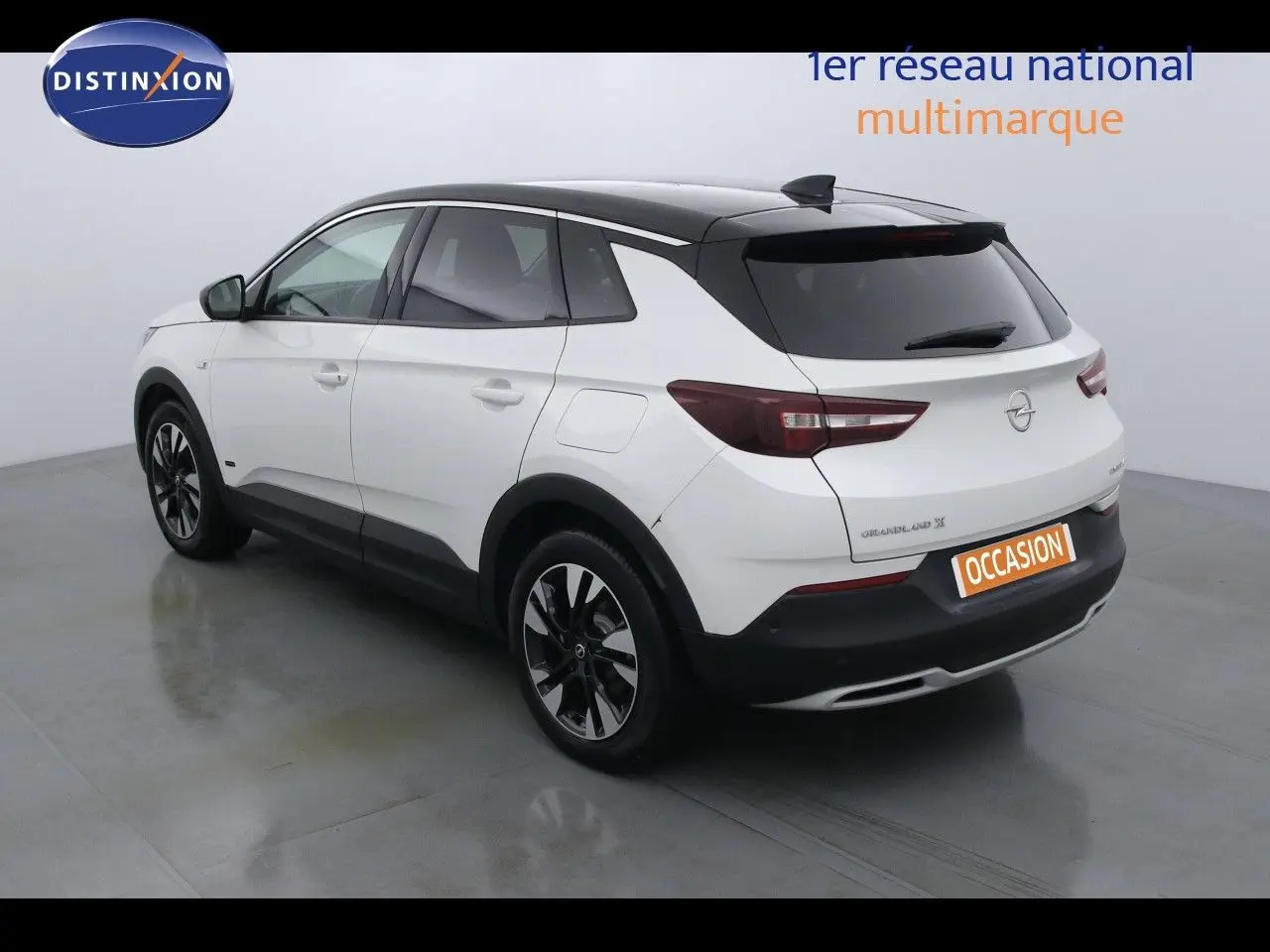 Opel Grandland X hybride blanc perle métal vu en 3/4 arrière côté gauche avec toit noir et jantes bicolores.