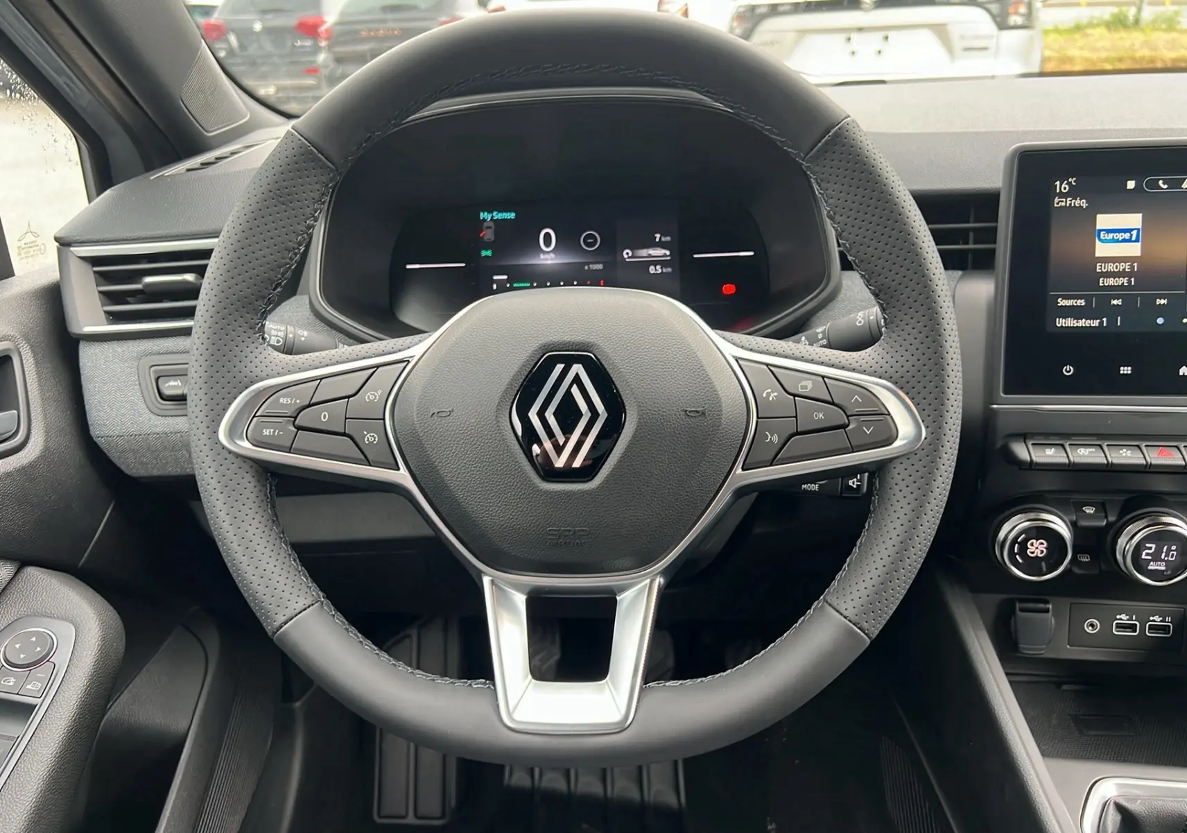 Vue intérieure centrée sur le volant perforé de la Renault Clio V TCE 90 Techno 2025 avec tableau de bord digital et écran tactile.