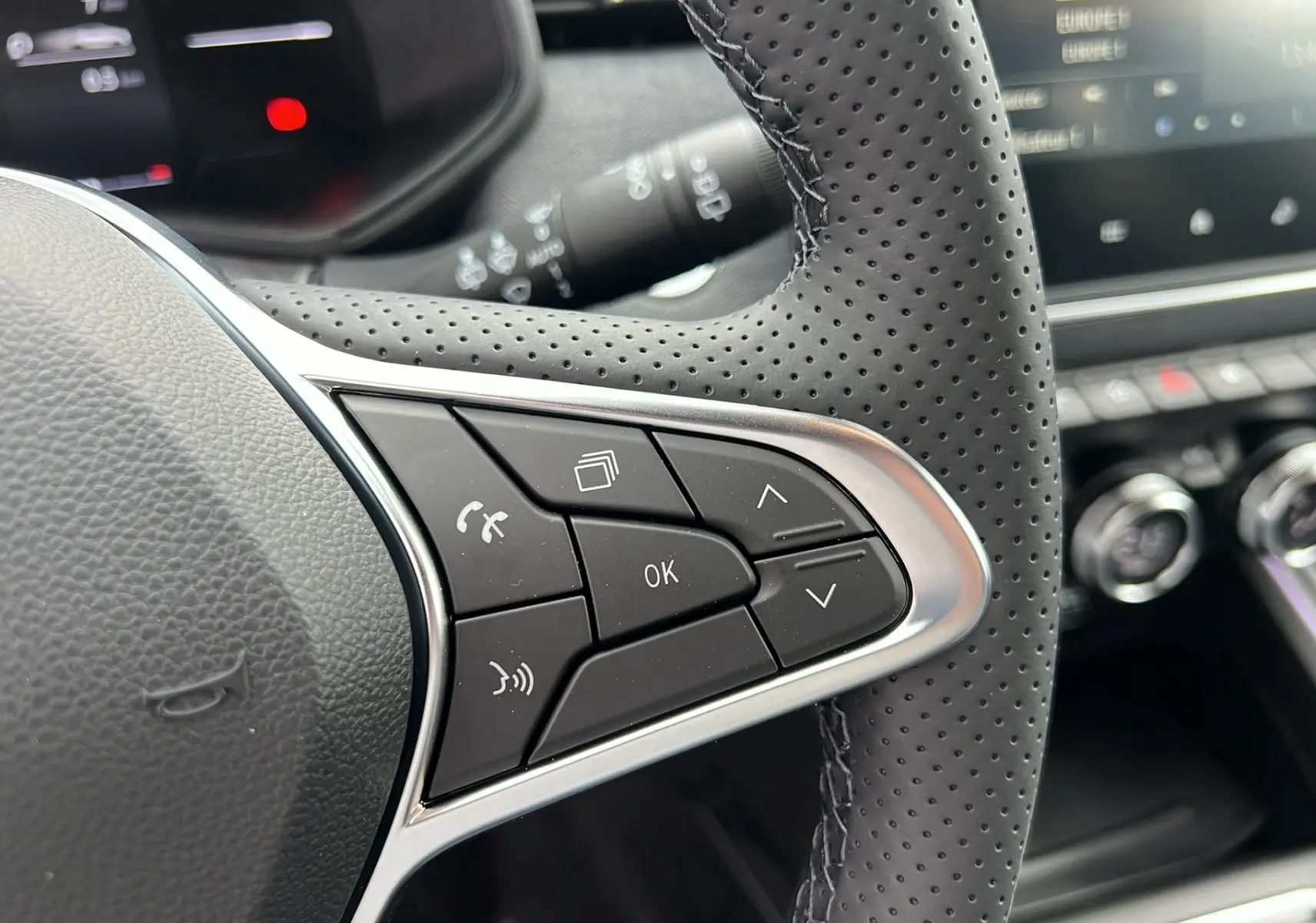 Gros plan sur les commandes au volant en cuir perforé de la Renault Clio V TCE 90 TECHNO 2025, tableau de bord en arrière-plan.
