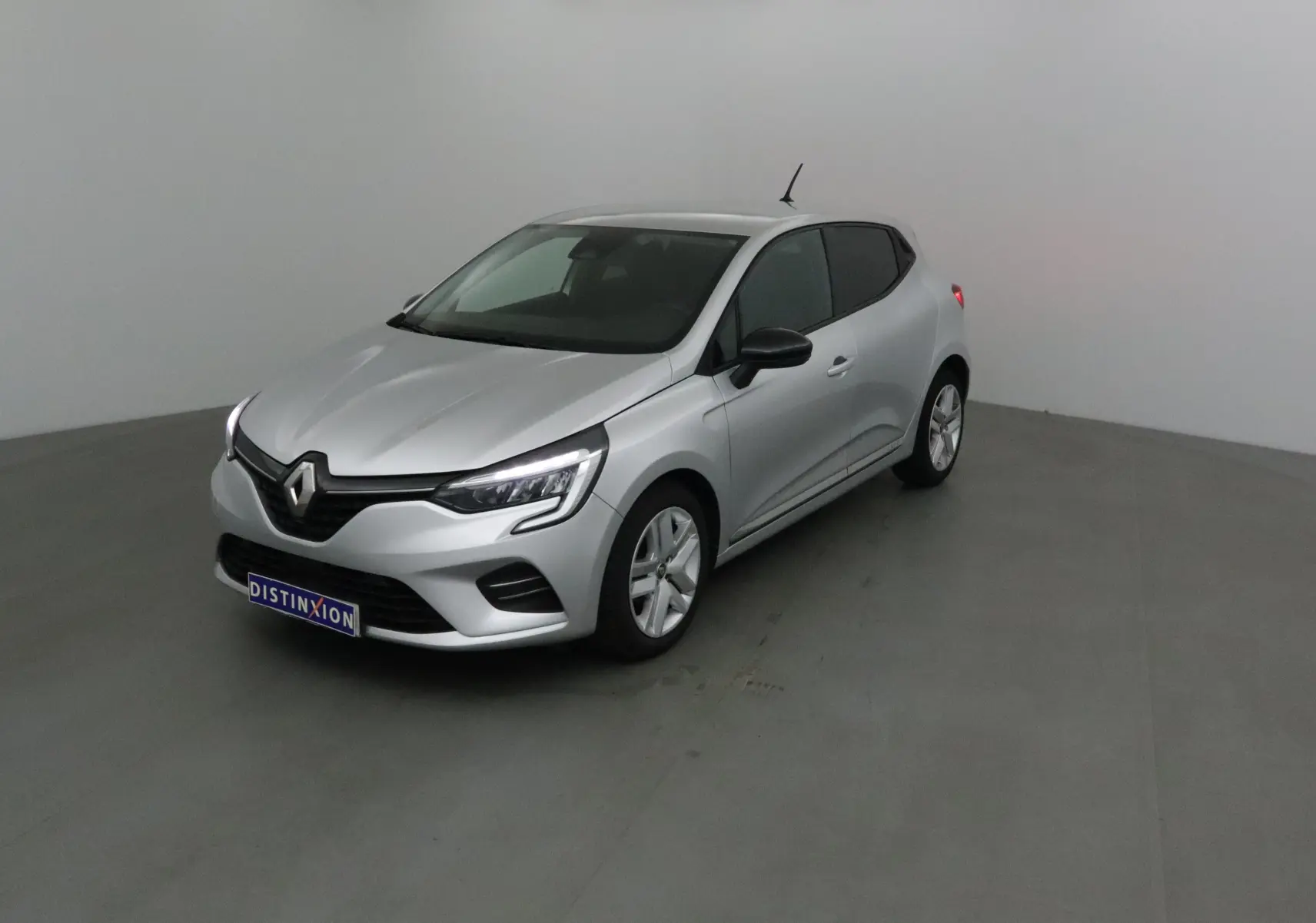 Renault Clio V gris platine vue 3/4 avant droit dans un studio, avec phares LED allumés et jantes alliage.