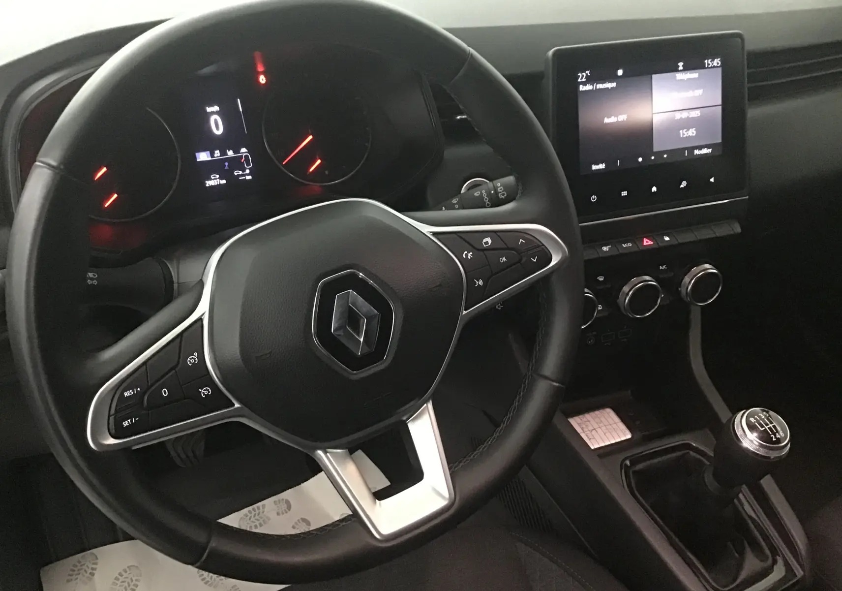 Vue intérieure du volant et tableau de bord d'une Renault Clio V gris platine avec boîte manuelle et écran tactile central.