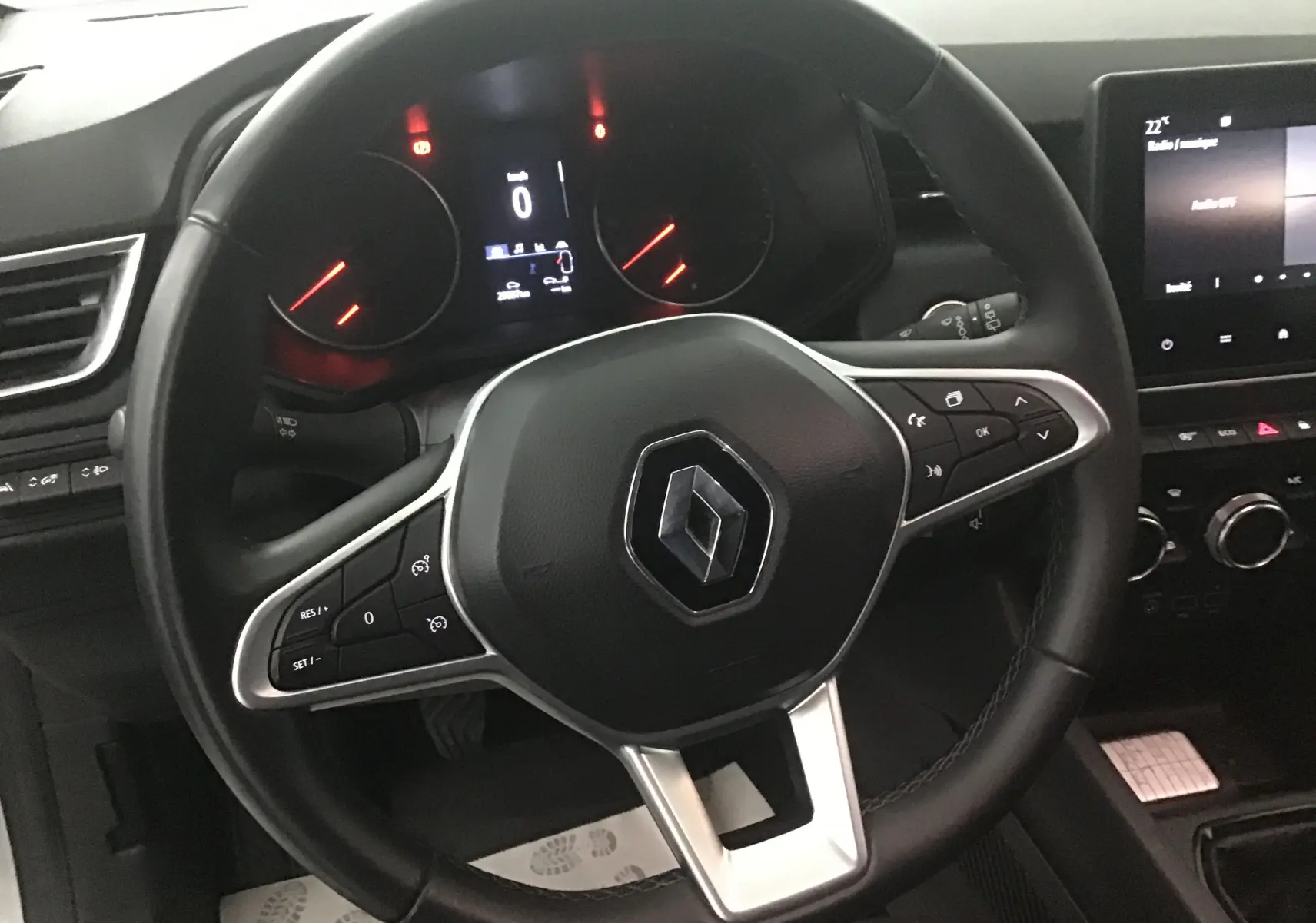 Vue rapprochée du volant noir de la Renault Clio V gris platine avec commandes intégrées et tableau de bord numérique.