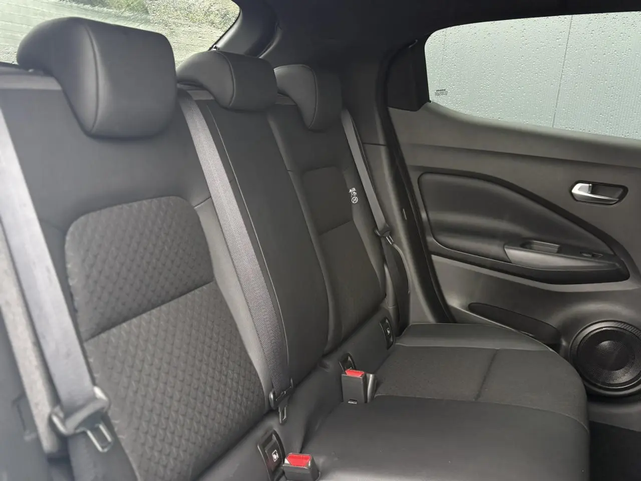 Vue latérale droite de la banquette arrière noire du Nissan Juke 2025 avec ceintures et haut-parleur intégré à la porte