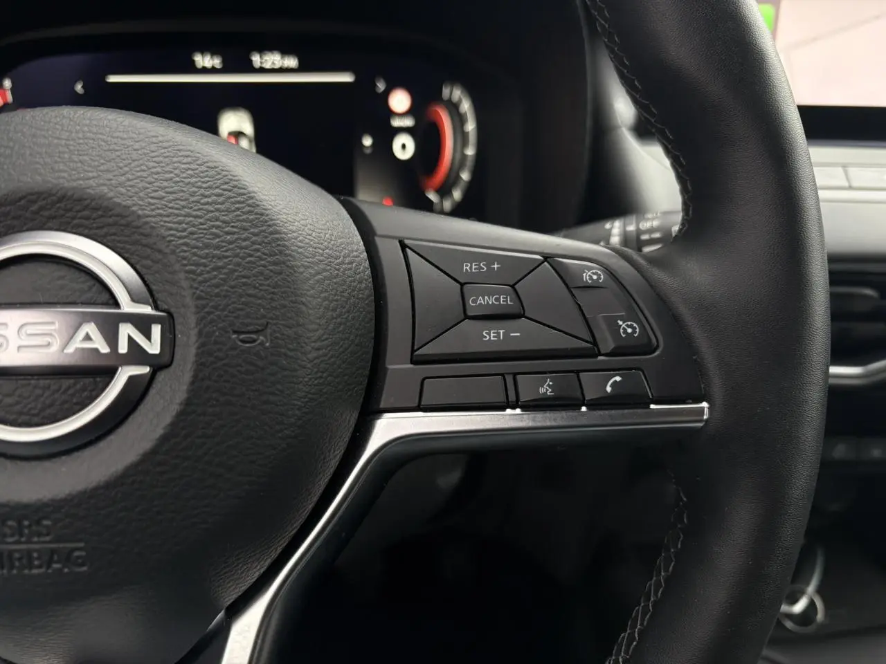 Gros plan sur le volant cuir noir du Nissan Juke blanc nacré 2025, avec commandes intégrées au côté droit.