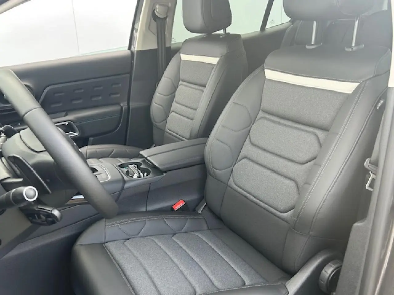 Intérieur avant du Citroën C5 Aircross 2025 avec sièges bi-matière gris et accoudoir central noir.