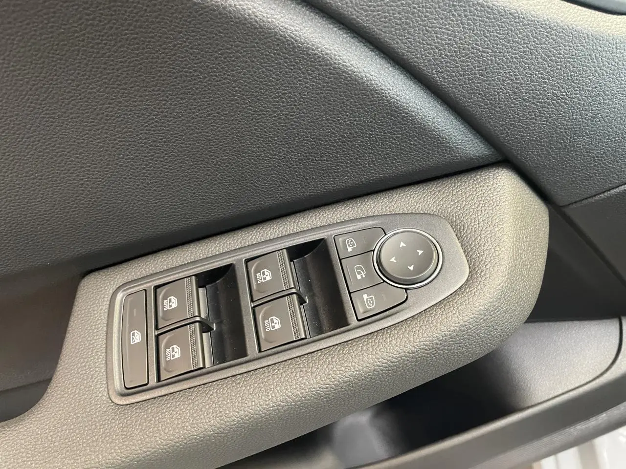 Commande des vitres électriques et réglage des rétroviseurs sur la porte côté gauche d'une Renault Clio gris Rafale.