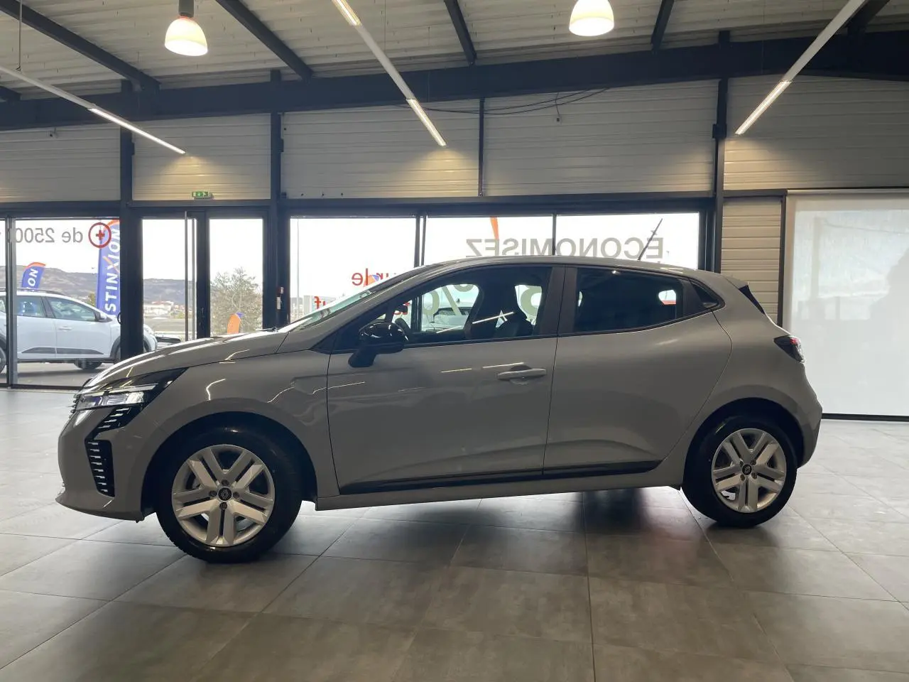 Profil côté gauche de la Renault Clio 1.5 Blue dCi 2025 gris Rafale en intérieur, avec jantes alliage et poignées couleur carrosserie.